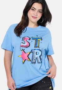 Světle modré bavlněné tričko s velkým černým, růžovým, žlutým a modrým nápisem "STAR" a grafikou hvězd, krátkými rukávy a volným střihem.