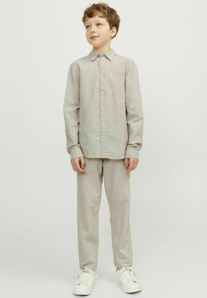 Camicia a maniche lunghe grigia chiaro con bottoni e pantaloni abbinati, realizzati in un tessuto morbido, abbinati a sneakers bianche, modello in piedi davanti a uno sfondo neutro.