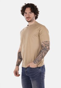 T-shirt beige a girocollo con maniche corte, realizzata in tessuto leggero, caratterizzata da un fit rilassato e dettagli di cucitura sottili.