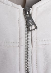 Tessuto in pelle bianca con una zip argentata. Presenta dettagli cuciti lungo le cuciture e un tirante della zip rotondo con un logo.