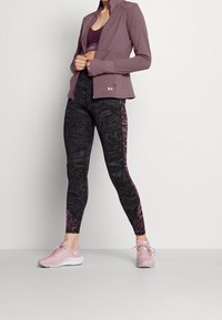 Purple zip-up athletic jacket over a dark patterned tank top, paired with black leggings featuring pink accents and matching pink sneakers.