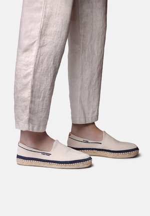 Plátené topánky bez šnúrok v béžovej farbe s modrými akcentmi a opletenou jutovou podrážkou. Zvršok má hladkú textúru a minimálne detaily.