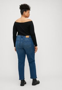 Top nero senza spalline abbinato a jeans denim blu con un'etichetta in pelle, tasche posteriori e risvolti, indossato con stivali neri.