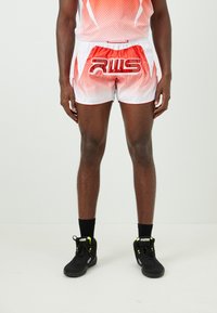 Male athlete wearing red and white sports shorts with "RWS" logo, black socks, and black athletic shoes with neon green accents, standing still.