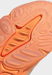 Kengänpohja, jossa on oranssi kumipinta, jossa on pyöreitä ja soikeita kuvioita, korostettuna läpinäkyvillä osioilla pitoa ja joustavuutta varten.