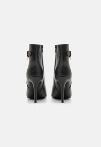 Μαύρες φουξ δερμάτινες μπότες αστραγάλου με κοφτή μύτη, τακούνι στιλέτο, πλαϊνούς φερμουάρ και χρυσές αγκράφες. Λείος υφή σε όλη την επιφάνεια.