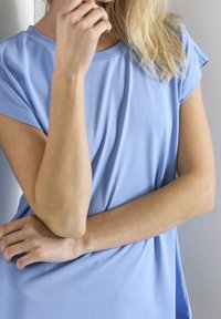 Jasnoniebieska bluzka z krótkim rękawem, z okrągłym dekoltem, gładką fakturą i lekko dopasowanym krojem, zaprezentowana z założonymi na siebie rękami.