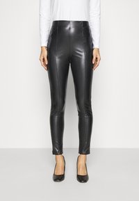 Černé kalhoty z faux kůže s vysokým pasem, úzkým střihem a středovými švy. Hladká textura, spárované s černými vysokými podpatky.