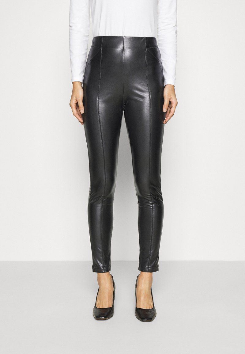 Černé kalhoty z faux kůže s vysokým pasem, úzkým střihem a středovými švy. Hladká textura, spárované s černými vysokými podpatky.