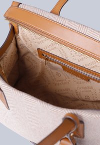 Beige kangaskassi, jossa on herringbone-kuvio, ruskeat nahkaosat, vetoketjukiinnitys ja vuorattu sisus, jossa on kohokuvioitu brändityyli.