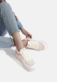 Sneaker con una toma crema e accenti rosa e viola pastello, suola testurizzata e zona delle dita perforata per la traspirazione.
