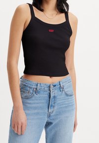 Černý žebrovaný top na ramínka s tenkými popruhy, se malým červeným logem Levi's. V kombinaci se světle modrými džíny s vysokým pasem.