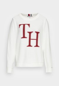 Pull en tricot blanc avec un grand logo rouge "TH" sur le devant, poignets et ourlet côtelés, et un col rond classique.