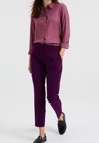 Lila skräddarsydda byxor kombinerat med en texturerad mauve knäppskjorta. Outfiten har en krage och uppvikta ärmar, accentuerad med svarta skor.