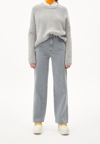 Suéter de canalé gris claro con un cuello redondo, combinado con unos jeans rectos gris claro de talle alto y zapatillas blancas con cordones amarillos.