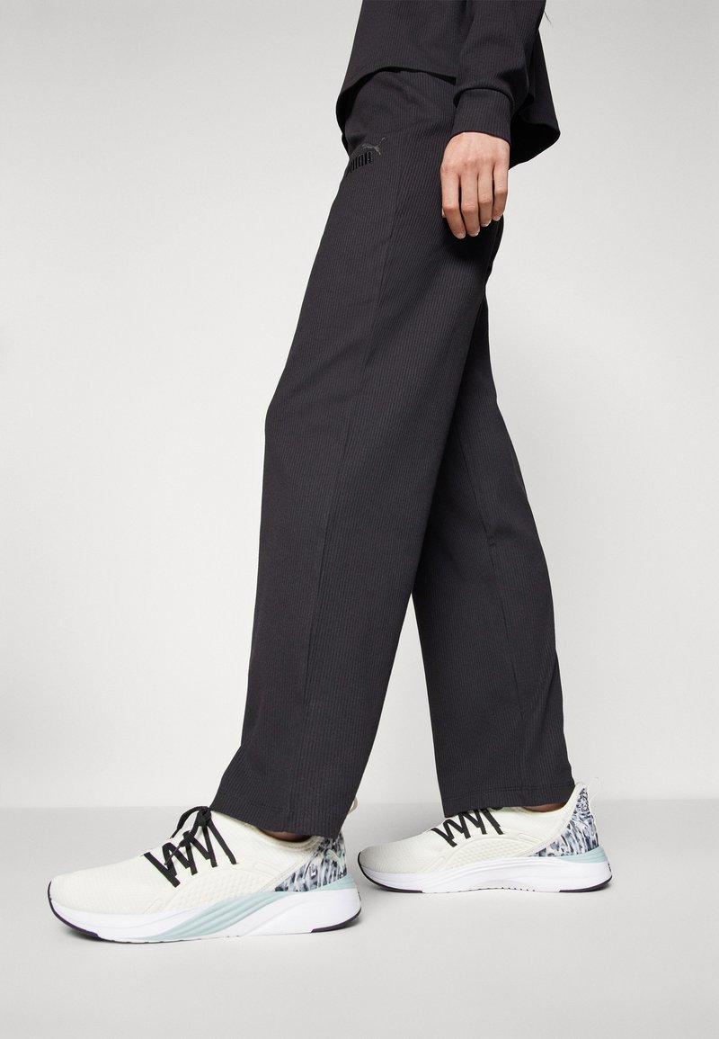 Pantaloni neri a coste e scarpe da ginnastica bianche con un accento azzurro chiaro e un dettagliato tallone testurizzato, con lacci neri e sezioni in rete.