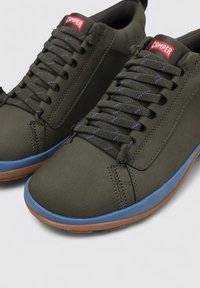 Sneakers verde scuro con suole in gomma blu e suole esterne marroni. Le caratteristiche includono lacci piatti e un logo sulla lingua. Finitura in materiale liscio.