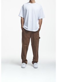 Biała bawełniana koszulka o luźnym kroju, zestawiona z brązowymi spodniami typu cargo z bocznymi kieszeniami oraz białymi trampkami. Gładka faktura, codzienny styl.
