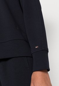 Námořnická mikina s žebrovanými manžetami, na hrudi s vyšívaným logem a s brandovaným akcentem na rukávu. Měkká textilní struktura.