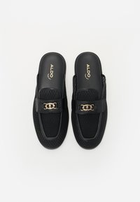 Sorte slip-on sko med en struktureret overdel, glatte læderdetaljer og en guldkæde. Designet til afslappet brug.