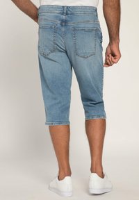 Pantalones capri de mezclilla azul claro con un diseño ajustado, dobladillo enrollado y dos bolsillos traseros. Combinados con zapatillas blancas.