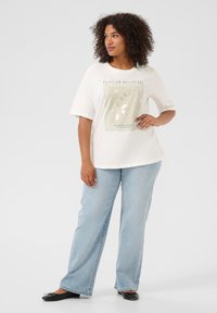 T-shirt blanc avec un motif imprimé de fleurs et du texte. Assorti avec un jean droit bleu clair et des ballerines noires.