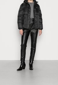 Zwarte pufferjas met een capuchon, gecombineerd met strakzittende zwarte lederen broek en hoge zwarte enkellaarsjes. Soepele textuur en slank ontwerp.