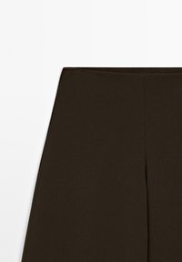 Bruna, högmidjade byxor tillverkade av ett mjukt, elastiskt material; har en ren, minimalistisk design utan synliga sömmar.