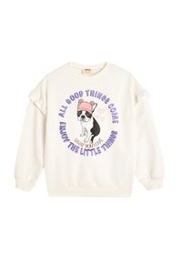 Sudadera blanca con acentos de volantes en las mangas, que presenta un gráfico de un perro con un sombrero rosa y texto morado que dice "Todo lo bueno llega."