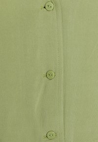 Camicia verde chiaro con bottoni abbinati, dettagli cuciti e un tessuto liscio e texturizzato.
