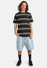 Camiseta de rayas negras con rayas horizontales blancas, combinada con shorts de carga azul claro. Zapatillas negras y calcetines cortos negros completan el look.