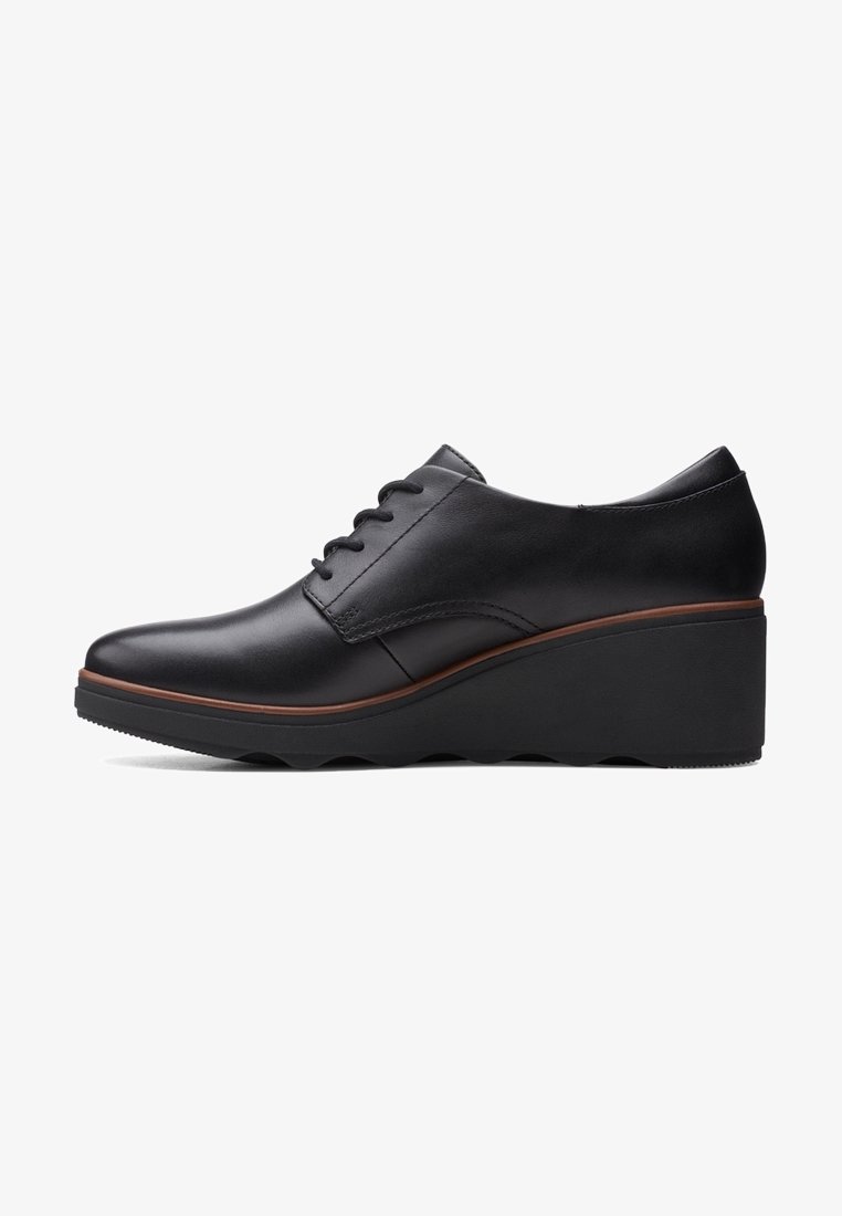 Chaussure compensée pour femme en cuir noir à lacets, avec une bordure marron le long de la semelle et une semelle extérieure en caoutchouc noir légèrement rainurée.