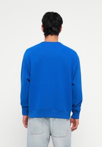 Felpa blu con scollo rotondo e maniche lunghe, realizzata in un tessuto a trama. La parte posteriore presenta un design semplice senza grafiche.