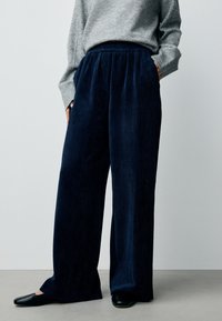 Pantaloni a gamba larga in velluto a coste blu navy con fascia elastica in vita. Una superficie testurizzata aumenta l'interesse visivo. Abbinati a ballerine nere e a un maglione grigio.