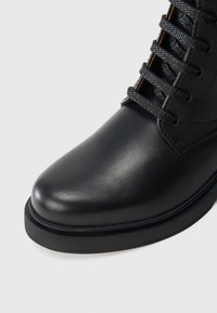 Μαύρη δερμάτινη μπότες έως τον αστράγαλο με στρογγυλή μύτη, υφή και μαύρα κορδόνια. Διαθέτει ανθεκτική, επίπεδη, καουτσούκ σόλα.