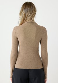 Bluzka z długim rękawem w jasnobrązowym kolorze, o dopasowanym kroju i gładkiej fakturze. Klasyczny styl z prostym dekoltem, wykonana z miękkiego materiału.