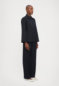Mörkblå tvådelad outfit bestående av en lös, kragärmad topp med långa ärmar och vida byxor, båda med subtila vertikala ränder.