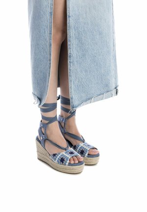 Alpargatas de cuña trenzadas en azul con correas al tobillo, que presentan patrones florales en la parte superior y una cuña envuelta en yute.