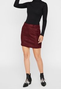 Mini-jupe en suede bourgogne avec une texture lisse, associée à un pull roulé noir et des bottines à chevilles avec des accents de flamme.