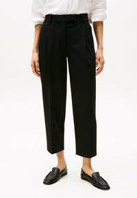 Zwarte op maat gemaakte broeken met een hoge taille, geplooide voorkant en een cropped lengte. Gladde stof en zijzakken. Gecombineerd met zwarte instappers.