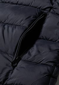 Navy puffjacka av tyg med kviltad textur. Har en horisontell dragkedjeöppning, slät yta och en robust svart dragkedja.