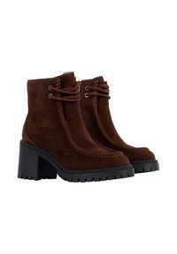 Botas de tobillo de ante marrón con un tacón negro grueso, cordones en la parte delantera y costuras decorativas en contraste a lo largo de los bordes.