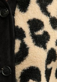 Black buttons on woolen fabric with beige and black leopard print pattern and black solid fabric panel.