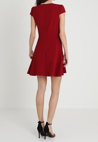 Vestido rojo de manga corta con falda acampanada, confeccionado en una tela suave, que presenta un cuerpo ajustado y un sutil detalle de costura en la parte posterior. Zapatos de tacón alto negros.