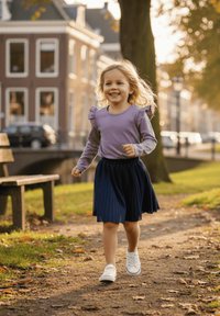 Dziecko ubrane w jasnofioletową bluzkę z długim rękawem i falbanami oraz granatową plisowaną spódnicę, w białych trampkach, biegnące ścieżką.