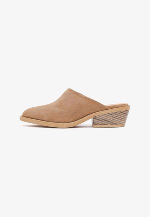 Mule de mujer en ante color cuero con talón bajo de bloque de madera apilada y puntera en forma de almendra sobre fondo blanco.