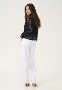Black lace blouse with long sleeves, featuring intricate patterns, paired with high-waisted white wide-leg trousers and nude high heels.