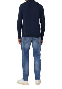 Marineblauer Strickpullover mit hohem Kragen, kombiniert mit hellblauen Denim-Jeans. Der Pullover hat gerippte Bündchen und Saum sowie detaillierte Gesäßtaschen an den Jeans.