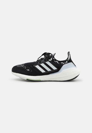 Czarne buty sportowe z białą podeszwą środkową, teksturowaną cholewką, trzema białymi paskami po boku i wzorzystymi akcentami w pobliżu palców.