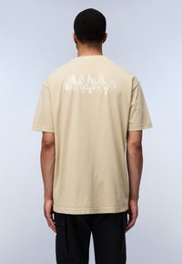 Camiseta de algodón beige con un gráfico de bosque en la parte trasera y mangas cortas. Tejido texturizado con un corte relajado.